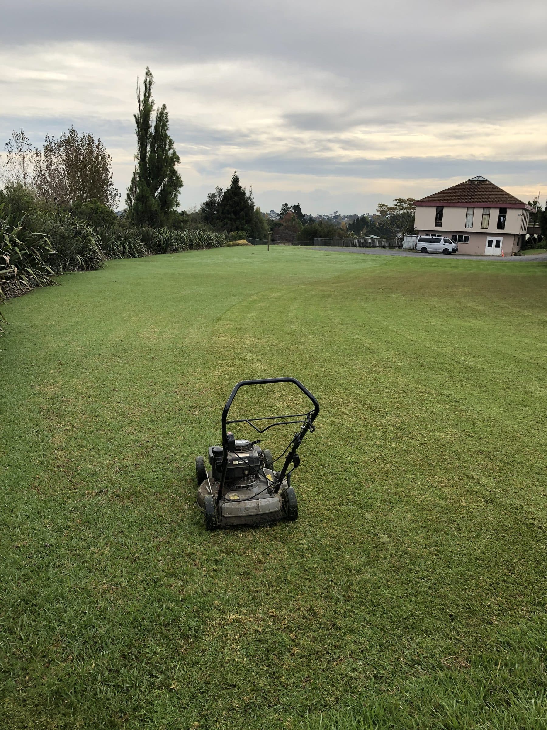 A push mower on a large open lawn area at dusk